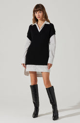 A woman is wearing a white shirt with thin black vertical stripes beneath a black sleeveless knit sweater vest. The shirt extends below the vest, creating a layered look, and the hem of the shirt is slightly longer in the back. She is also wearing a short, matching striped skirt and knee-high black patent leather boots.
